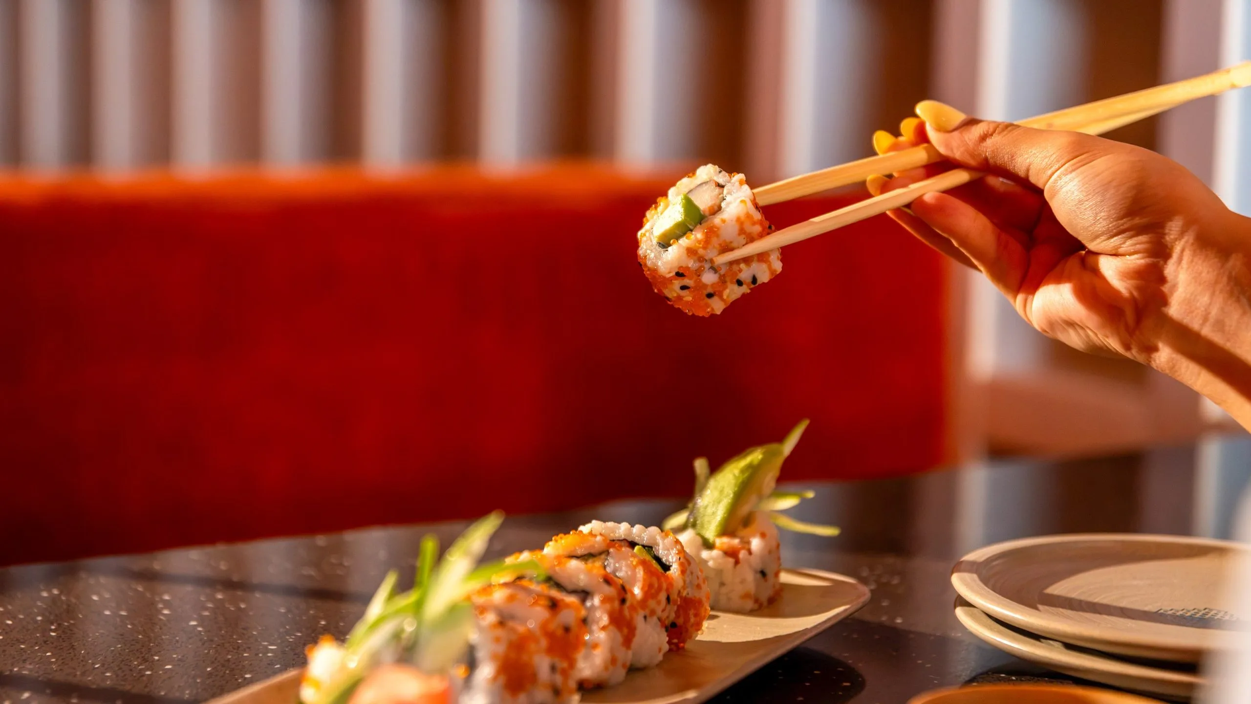 A hand lifting a sushi roll from a board on the counter