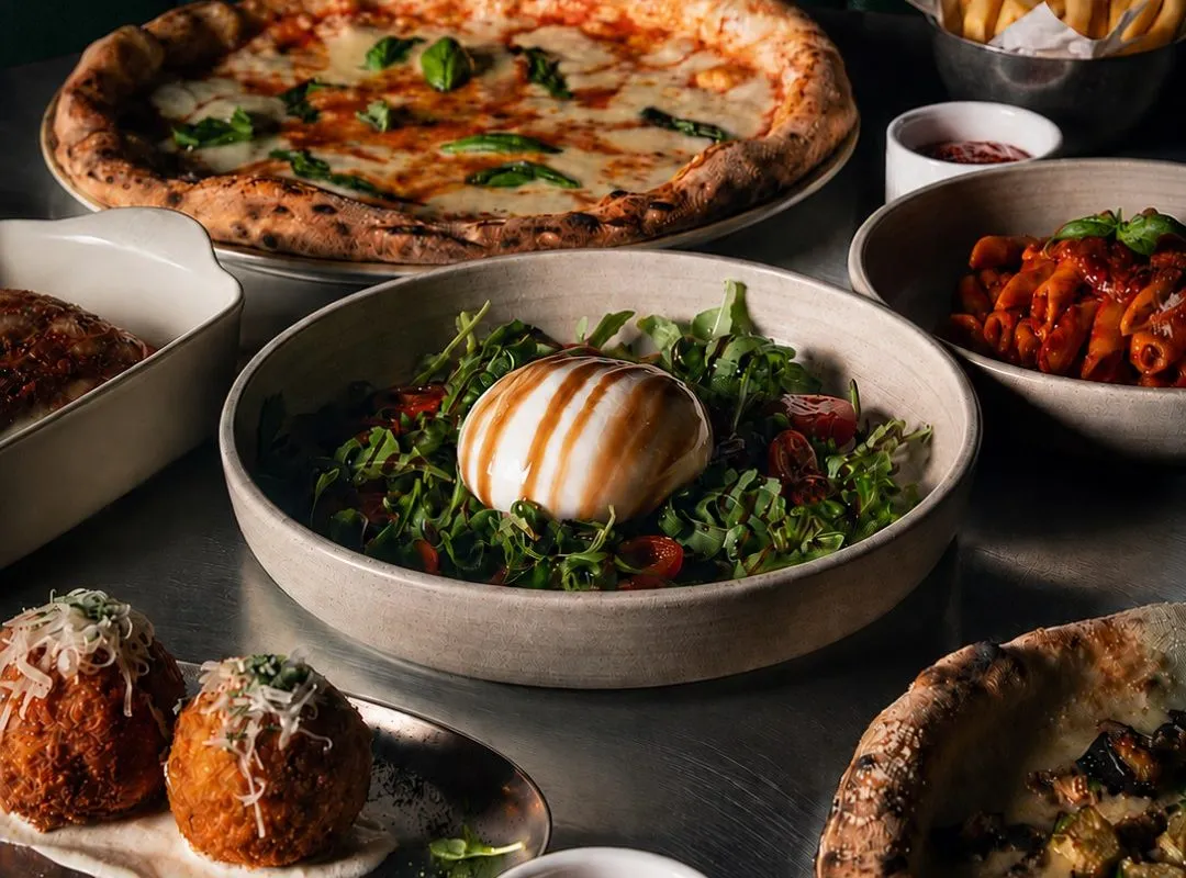 A shared table of pizza, salads and small plates